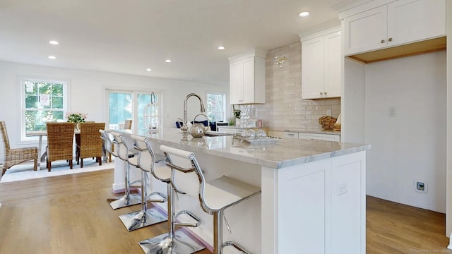 12 Woodland Dr, Milford, CT 06460 - kitchen featuring recessed lighting, decorative backsplash, light wood-type flooring, white cabinetry, and a kitchen island with sink