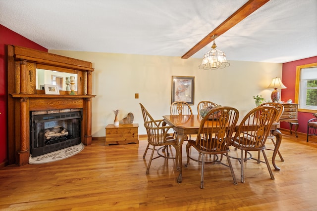 dining area featuring light wood-style floors, a chandelier, a fireplace with flush hearth, and beam ceiling