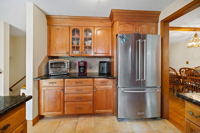 kitchen with high end refrigerator, dark stone counters, brown cabinetry, and a textured ceiling