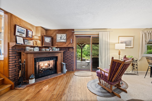 living room with a warm lit fireplace, a textured ceiling, hardwood / wood-style flooring, wooden walls, and stairs