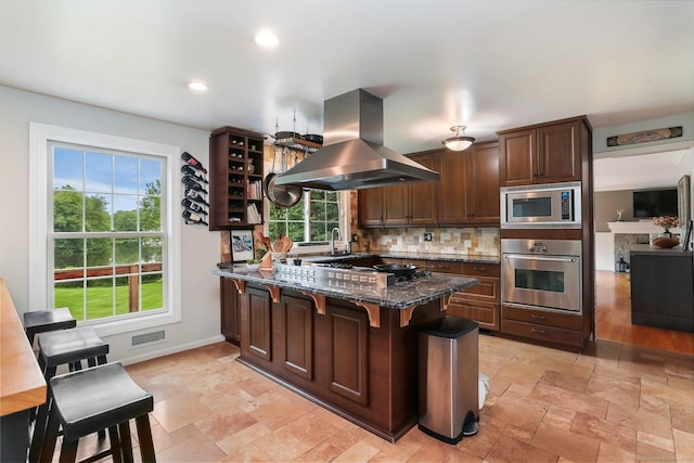 101 Golden Hill St, Trumbull, CT 06611 - kitchen featuring appliances with stainless steel finishes, island exhaust hood, a peninsula, tasteful backsplash, and dark stone countertops