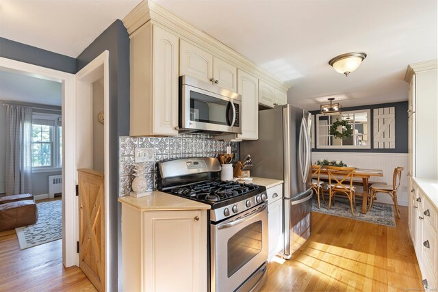 216 Main St, Glastonbury, CT 06073 - kitchen featuring appliances with stainless steel finishes, radiator, light wood-type flooring, light countertops, and a wainscoted wall