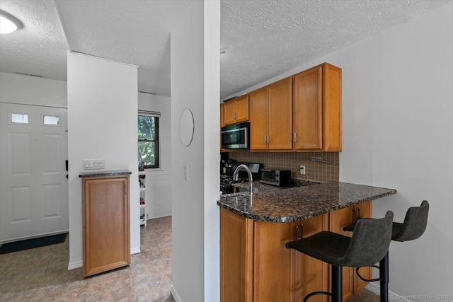 125 Olive St Apt D2, New Haven, CT 06511 - kitchen with stainless steel microwave, brown cabinets, backsplash, a kitchen breakfast bar, and dark stone counters