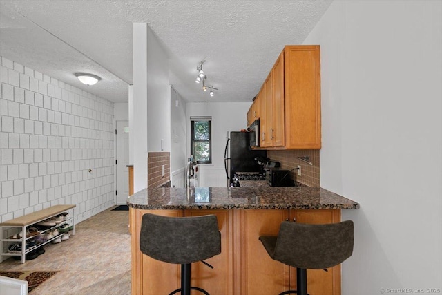 125 Olive St Apt D2, New Haven, CT 06511 - kitchen with tile walls, a peninsula, dark stone countertops, a textured ceiling, and stainless steel microwave