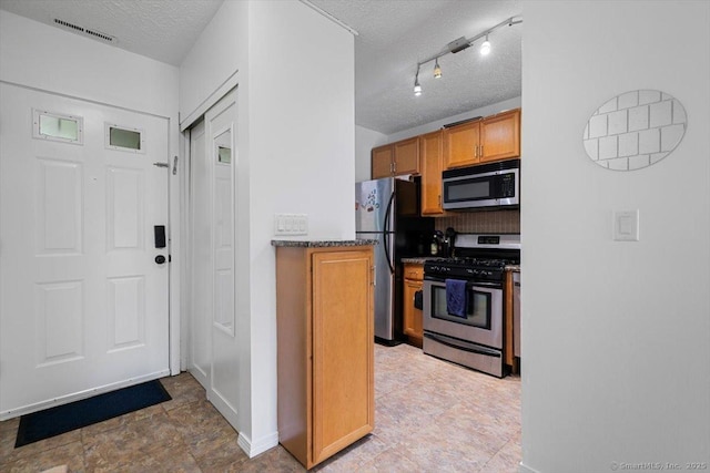 125 Olive St Apt D2, New Haven, CT 06511 - kitchen with appliances with stainless steel finishes, a textured ceiling, decorative backsplash, brown cabinetry, and dark stone countertops