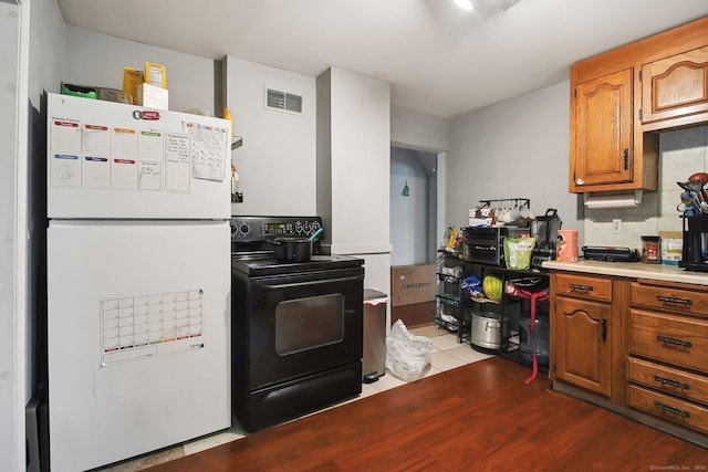 32 Williams St, Bristol, CT 06010 - kitchen with freestanding refrigerator, black electric range oven, light countertops, brown cabinets, and light wood-type flooring