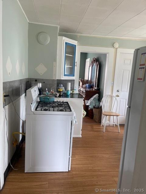 561 E St, New Britain, CT 06051 - kitchen featuring white gas stove, freestanding refrigerator, wood finished floors, ornamental molding, and glass insert cabinets