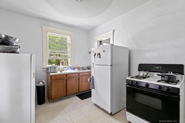 212 Maple St, New Haven, CT 06511 - kitchen with range with gas cooktop, freestanding refrigerator, white refrigerator with ice dispenser, brown cabinetry, and light countertops