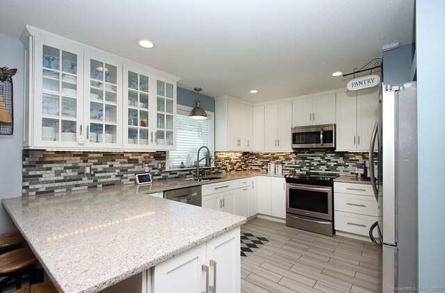 362 Main St, Meriden, CT 06451 - kitchen featuring appliances with stainless steel finishes, a peninsula, white cabinetry, decorative backsplash, and recessed lighting