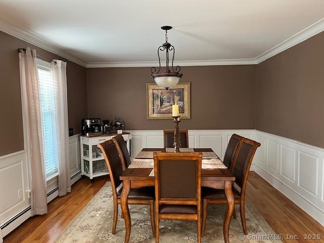 47 Merwin Brook Rd, Brookfield, CT 06804 - dining room with light wood finished floors, crown molding, wainscoting, a baseboard heating unit, and a decorative wall
