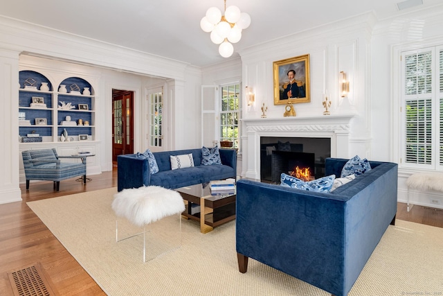 354 S Ave, New Canaan, CT 06840 - living area with ornamental molding, light wood-style flooring, a warm lit fireplace, a chandelier, and built in features