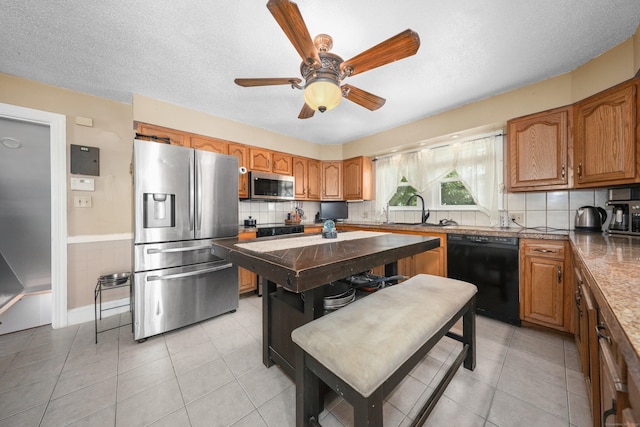 229 Hauser St, Waterbury, CT 06704 - kitchen featuring stainless steel appliances, light tile patterned flooring, ceiling fan, brown cabinetry, and tasteful backsplash