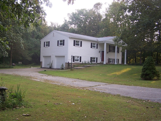 split foyer home with an attached garage, dirt driveway, a front lawn, and view of wooded area