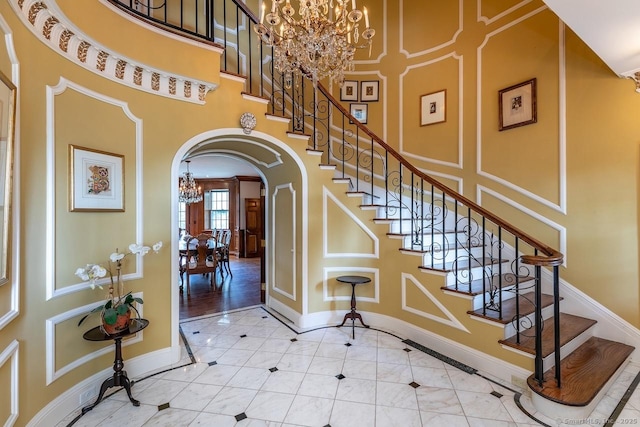 foyer featuring a chandelier, arched walkways, a towering ceiling, and stairway
