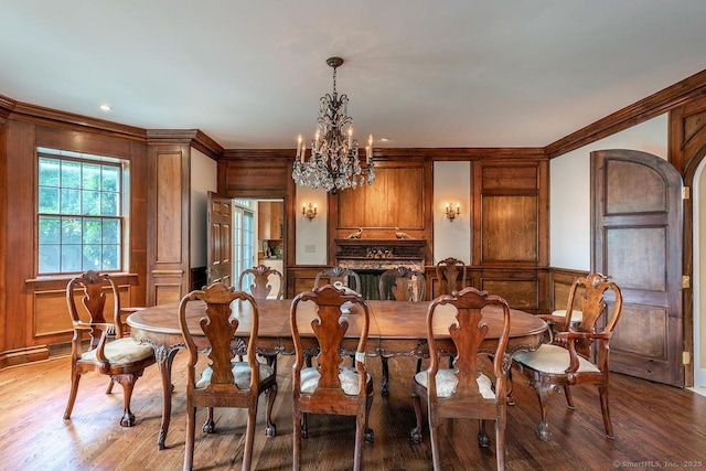 dining room featuring a chandelier, light wood-style flooring, crown molding, wainscoting, and a decorative wall