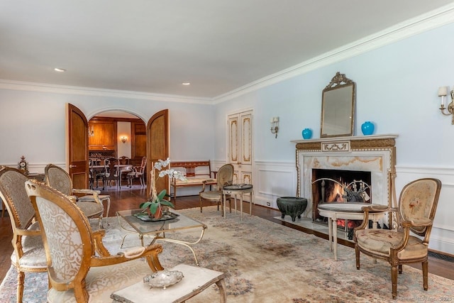 living room with arched walkways, ornamental molding, a wainscoted wall, a fireplace, and wood finished floors