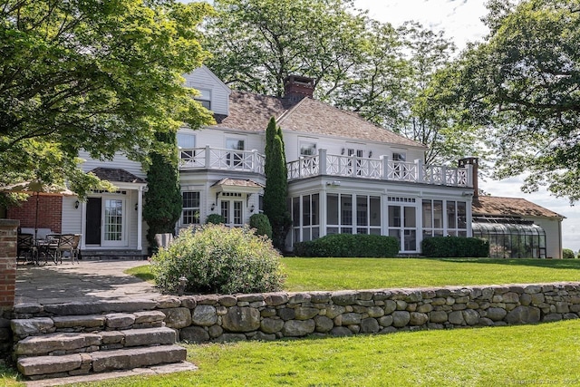 back of property featuring a balcony, a chimney, a patio area, a yard, and a sunroom