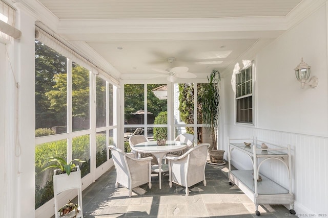 sunroom with a ceiling fan, a wainscoted wall, ornamental molding, stone finish flooring, and outdoor dining area
