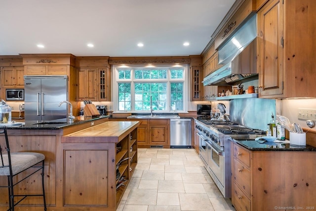 kitchen featuring high end appliances, open shelves, dark stone countertops, and recessed lighting