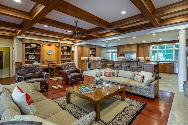 living area with ornate columns, coffered ceiling, beamed ceiling, a ceiling fan, and wine cooler
