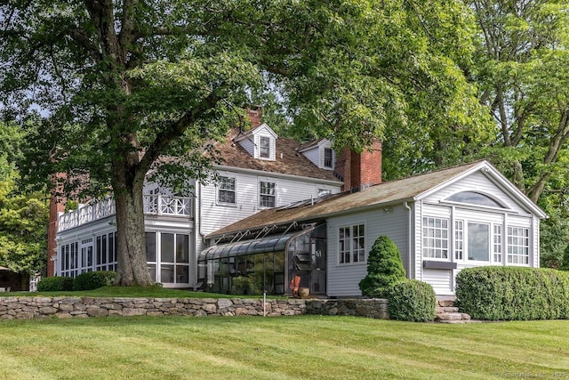 back of house with a sunroom, a chimney, and a lawn