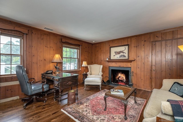 living room featuring wood finished floors, wood walls, a warm lit fireplace, and a desk