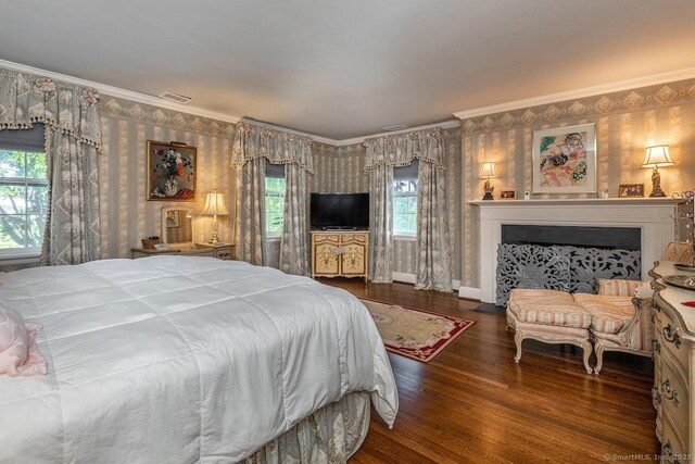 bedroom with wallpapered walls, crown molding, wood finished floors, and a fireplace with flush hearth