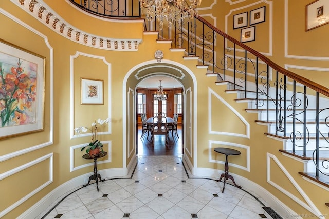 tiled foyer entrance featuring arched walkways, a chandelier, a high ceiling, stairs, and inlaid floor details
