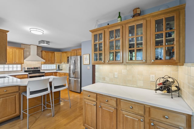 34 Joyce St, Guilford, CT 06437 - kitchen with wall chimney range hood, appliances with stainless steel finishes, a kitchen breakfast bar, decorative backsplash, and light wood-style flooring