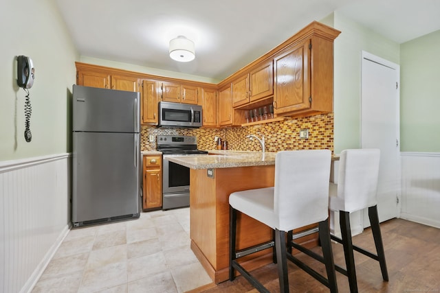 718 Cove Rd Apt 3, Stamford, CT 06902 - kitchen featuring appliances with stainless steel finishes, light countertops, a kitchen bar, a wainscoted wall, and a peninsula
