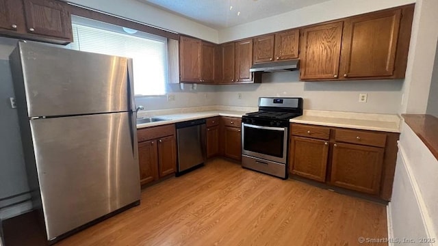 kitchen featuring appliances with stainless steel finishes, under cabinet range hood, light wood finished floors, and light countertops