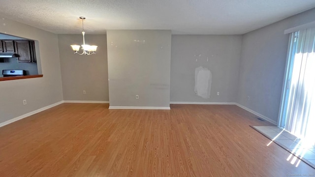 empty room featuring a chandelier, light wood finished floors, and a textured ceiling
