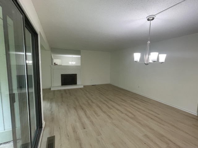 277 Heritage Vlg Unit C, Southbury, CT 06488 - unfurnished living room with a chandelier, light wood-type flooring, and a brick fireplace