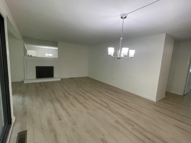 277 Heritage Vlg Unit C, Southbury, CT 06488 - unfurnished living room featuring a chandelier, light wood-style floors, a fireplace with raised hearth, and a textured ceiling