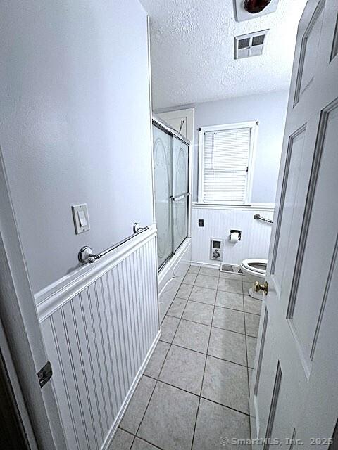 21 Eastwood Rd, Bridgeport, CT 06606 - bathroom featuring tile patterned flooring, enclosed tub / shower combo, wainscoting, and a textured ceiling