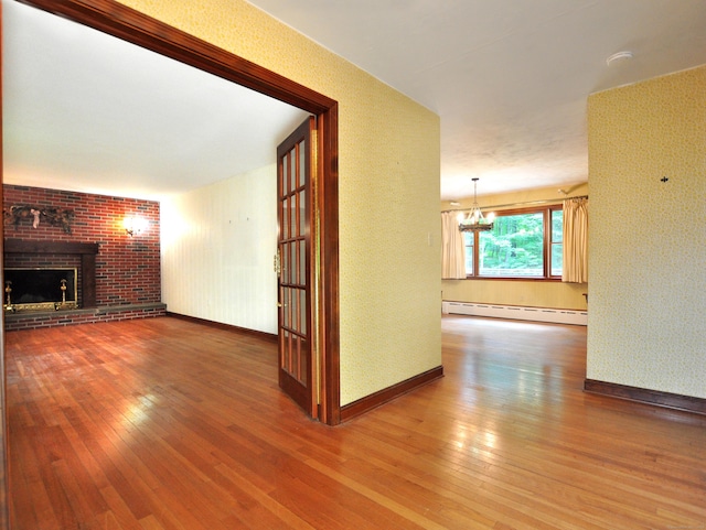 3 Carriage Dr, Canton, CT 06019 - unfurnished living room with a baseboard heating unit, a chandelier, wood-type flooring, a brick fireplace, and wallpapered walls