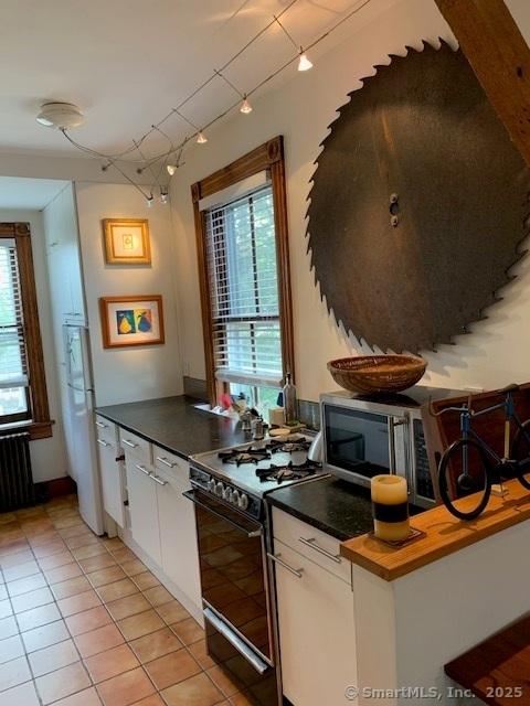 14 Jefferson St, Norwalk, CT 06851 - kitchen featuring black stove, rail lighting, light tile patterned floors, radiator heating unit, and white cabinets