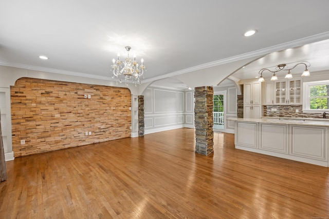 90 Haddad Rd, Waterbury, CT 06708 - unfurnished living room with decorative columns, arched walkways, light wood-style flooring, ornamental molding, and a chandelier