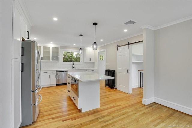 502 Adams St, Manchester, CT 06040 - kitchen featuring appliances with stainless steel finishes, a barn door, light countertops, white cabinetry, and tasteful backsplash