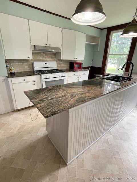 2 Judd Ave, Bethel, CT 06801 - kitchen with white gas range oven, under cabinet range hood, white cabinets, backsplash, and decorative light fixtures