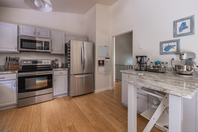 111 Nicole Dr, Milford, CT 06460 - kitchen featuring appliances with stainless steel finishes, light wood-style flooring, gray cabinetry, a towering ceiling, and light stone countertops