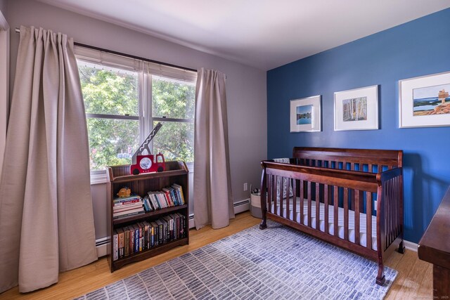 111 Nicole Dr, Milford, CT 06460 - bedroom with a crib, wood finished floors, baseboard heating, and a baseboard heating unit