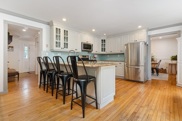 41 Arlington Rd, Stamford, CT 06902 - kitchen with stainless steel appliances, light wood finished floors, a kitchen bar, white cabinets, and ornamental molding