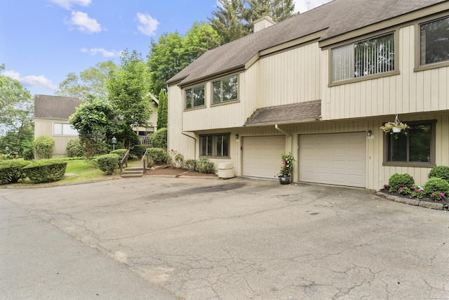 518 Iroquois Ln Unit A, Stratford, CT 06614 - view of property featuring asphalt driveway, roof with shingles, a chimney, and an attached garage