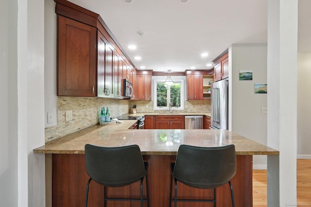 223 N St, Ridgefield, CT 06877 - kitchen featuring stainless steel appliances, a peninsula, backsplash, hanging light fixtures, and light wood-style flooring
