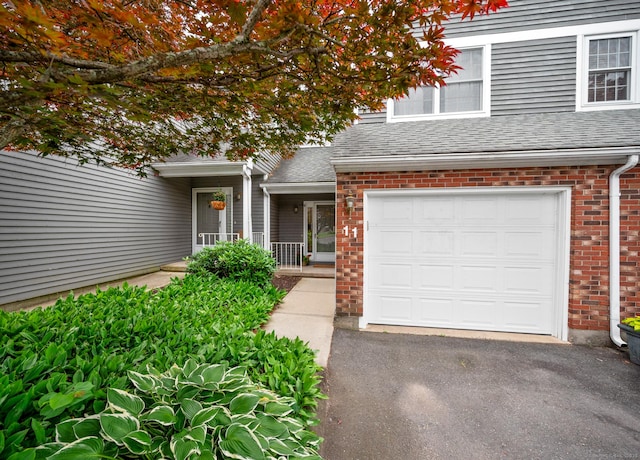 1325 Farmington Ave Apt 11, Bristol, CT 06010 - view of exterior entry featuring brick siding, an attached garage, a shingled roof, and driveway