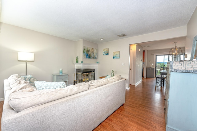 708 Lake Vista Dr Unit 708, East Hampton, CT 06424 - living room with a glass covered fireplace, a chandelier, wood finished floors, and a textured ceiling