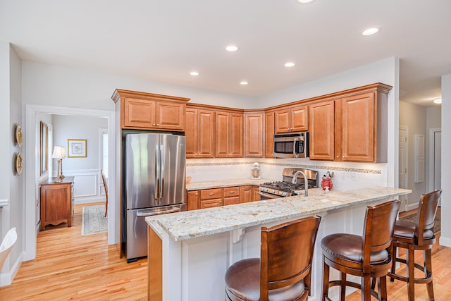 199 Meadow Brook Rd Unit 199, Oxford, CT 06478 - kitchen featuring stainless steel appliances, a peninsula, light wood-type flooring, a kitchen breakfast bar, and light stone counters