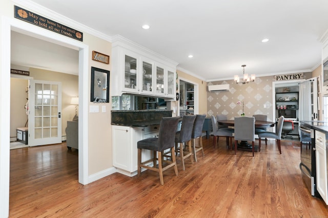 630 Fairview Ave, Bridgeport, CT 06606 - kitchen with a wall unit AC, white cabinetry, light wood-style flooring, wallpapered walls, and a chandelier