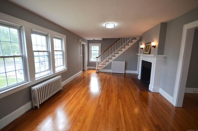 954 Birmingham St, Bridgeport, CT 06606 - unfurnished living room featuring radiator, wood finished floors, stairs, and a fireplace with flush hearth